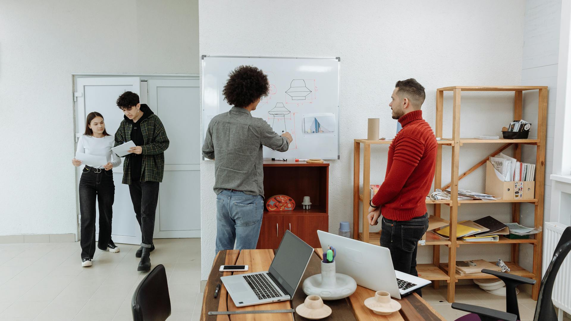 Diverse team collaborating in a modern office, discussing ideas with laptops and a whiteboard.