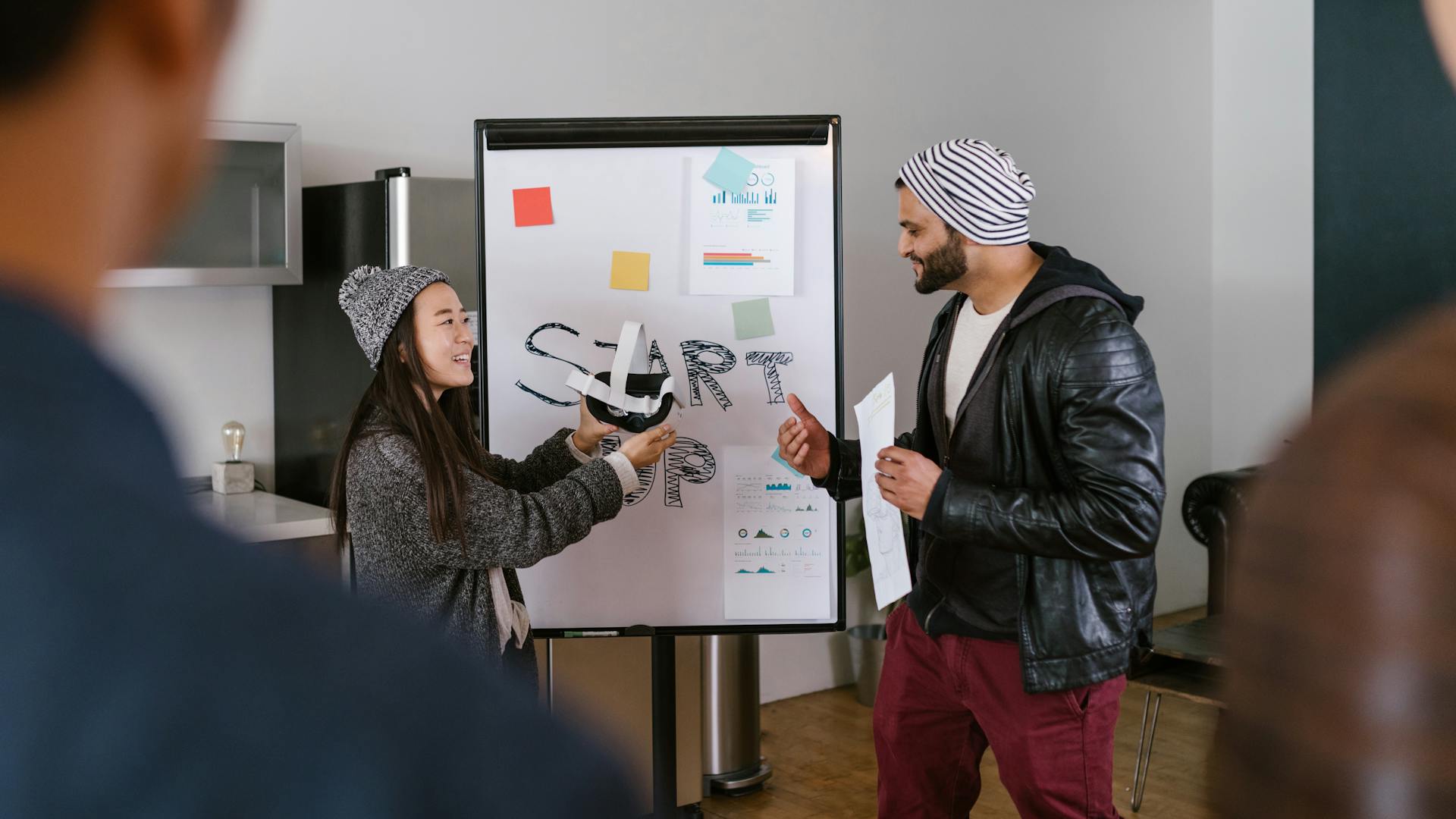 A diverse group of coworkers brainstorming in a modern startup environment, presenting ideas on a whiteboard.