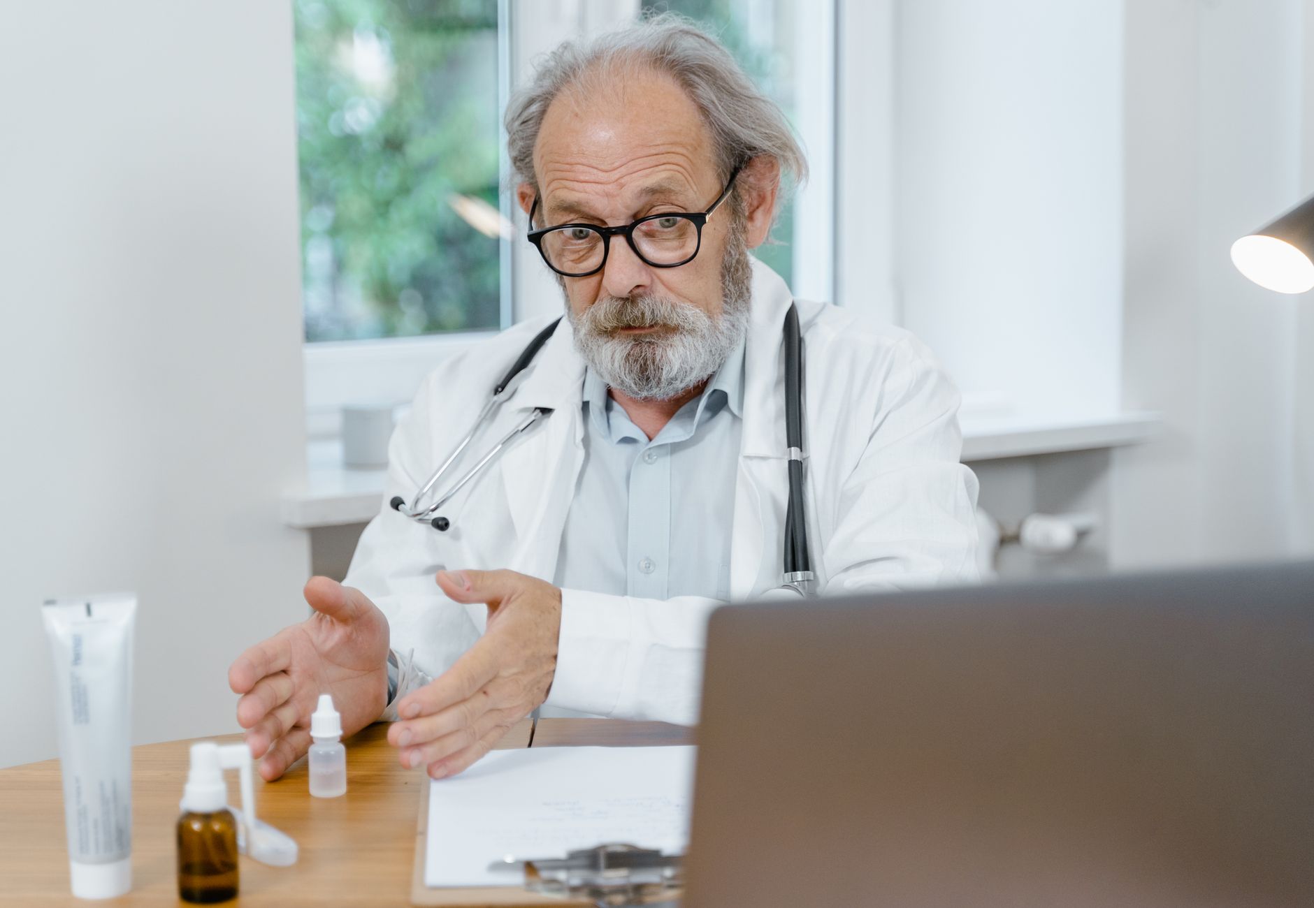 An elderly doctor in a white coat conducting an online medical consultation, focusing attentively.