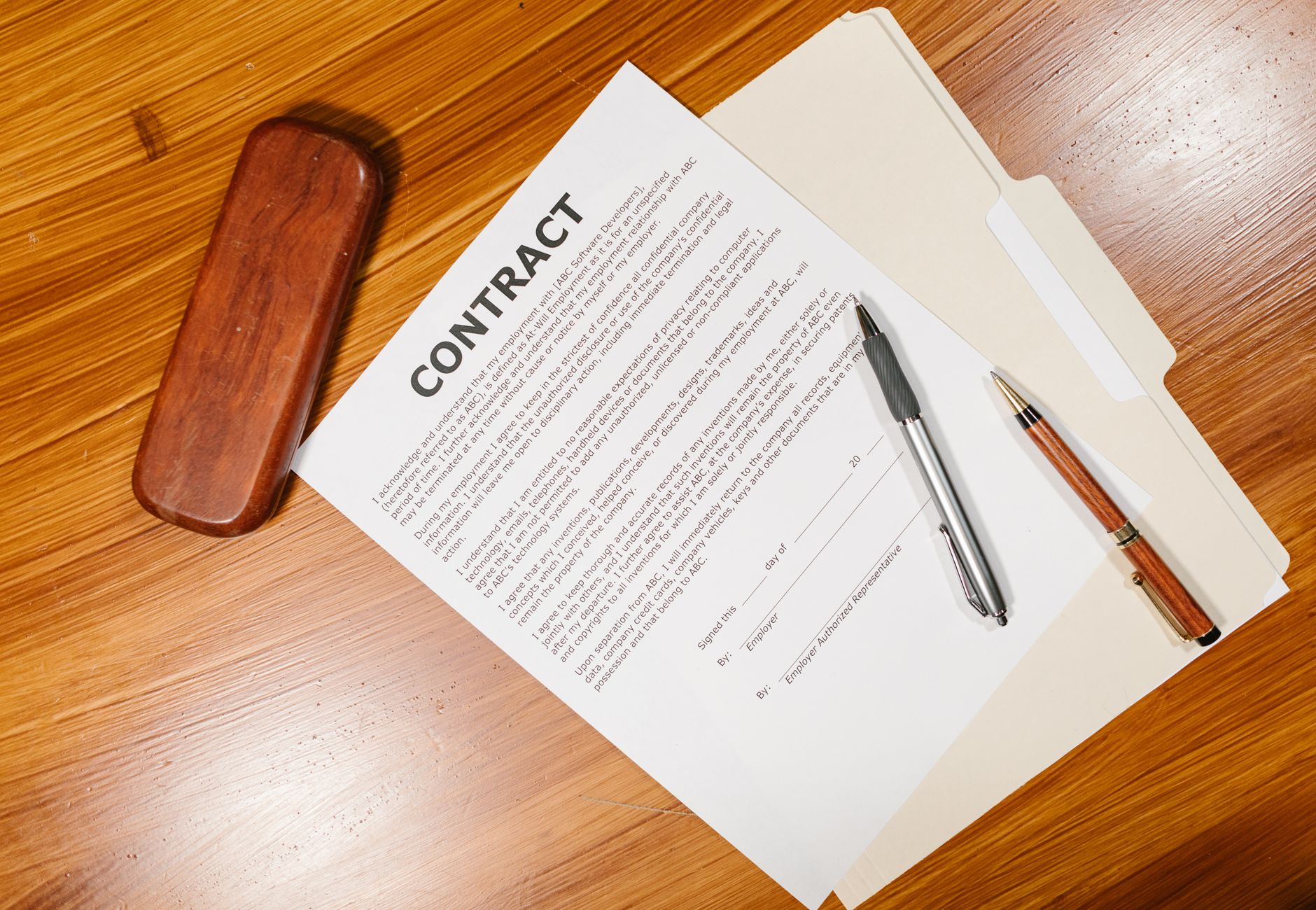 High-angle view of a contract document with pens and a case on a wooden table.