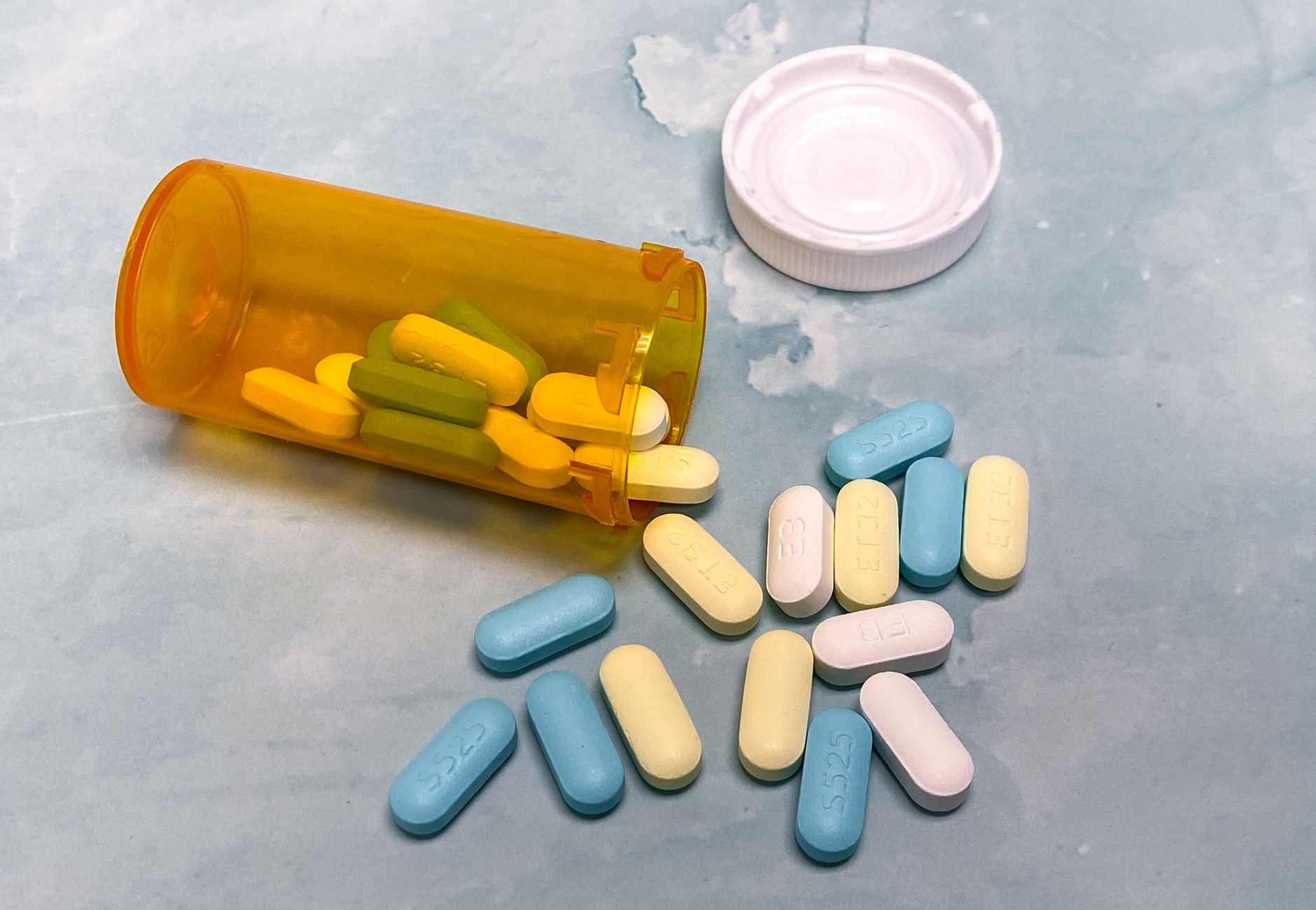 An open prescription bottle with assorted pills on a light blue background, high angle view.