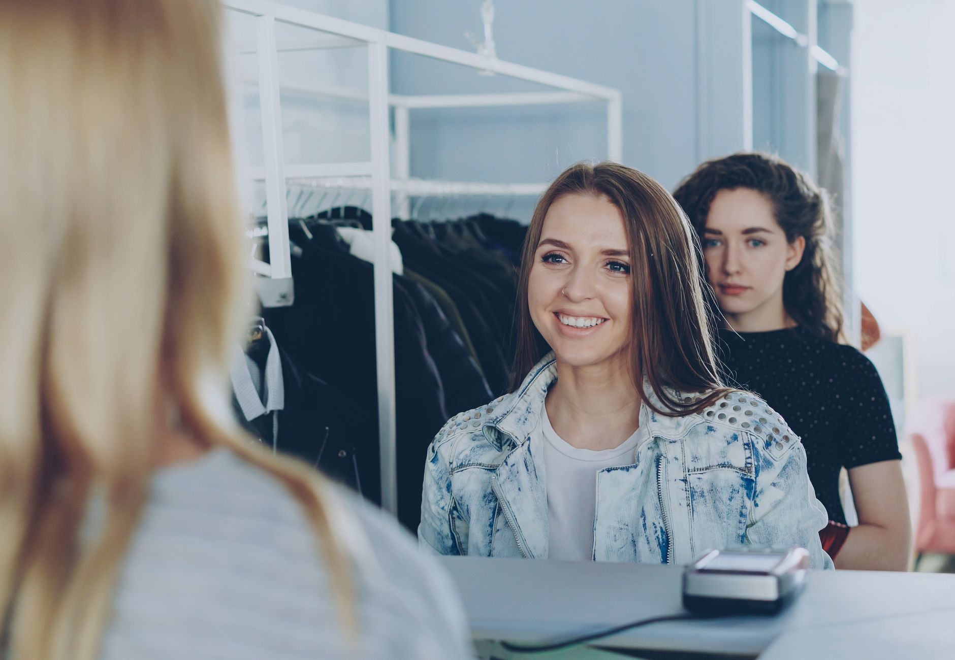 Two young women shopping and interacting with cashier in clothing store.