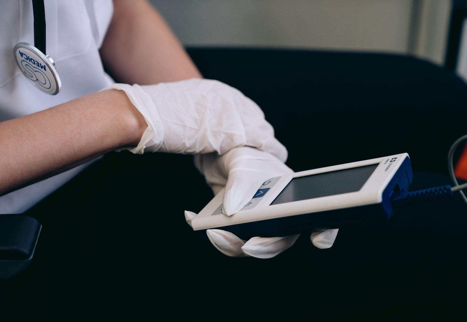 Healthcare worker with gloves using medical device indoors.