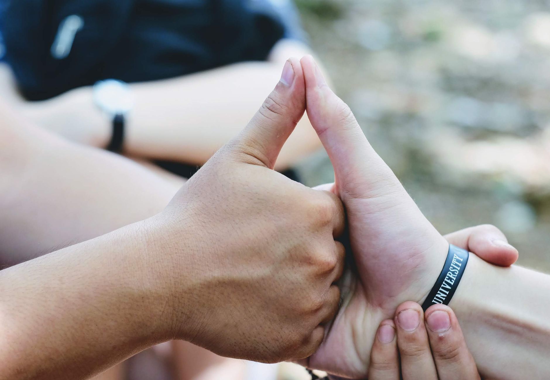 Close-up of hands forming a unity symbol, featuring diverse skin tones and a 'university' bracelet.