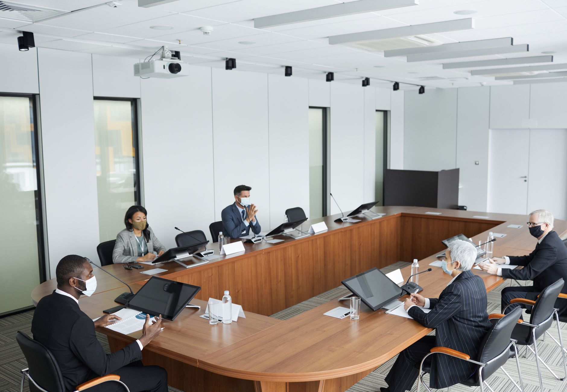 Business professionals wearing masks attending a conference meeting in a modern setting.