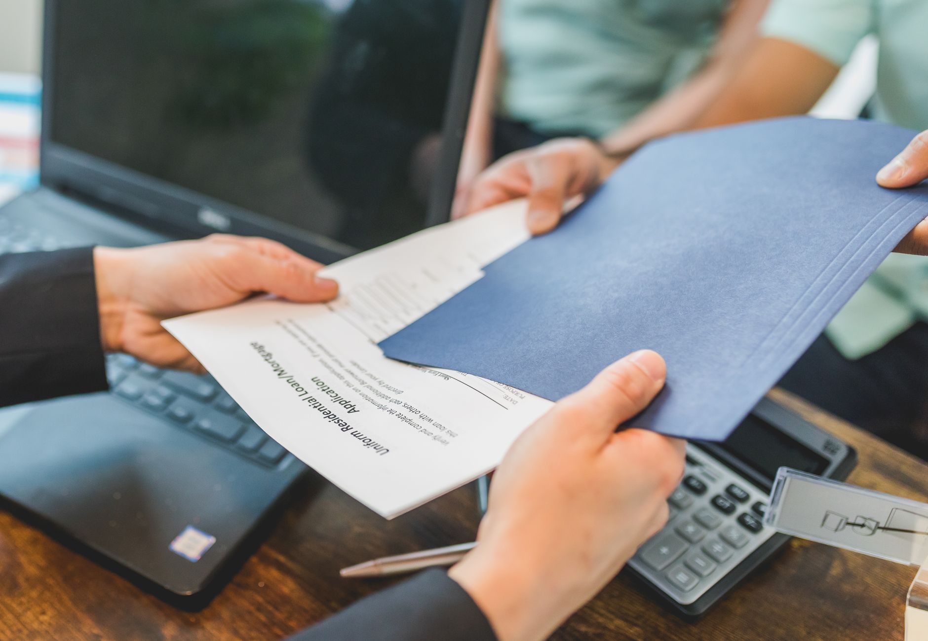 Close-up of hands exchanging real estate documents in an office setting.