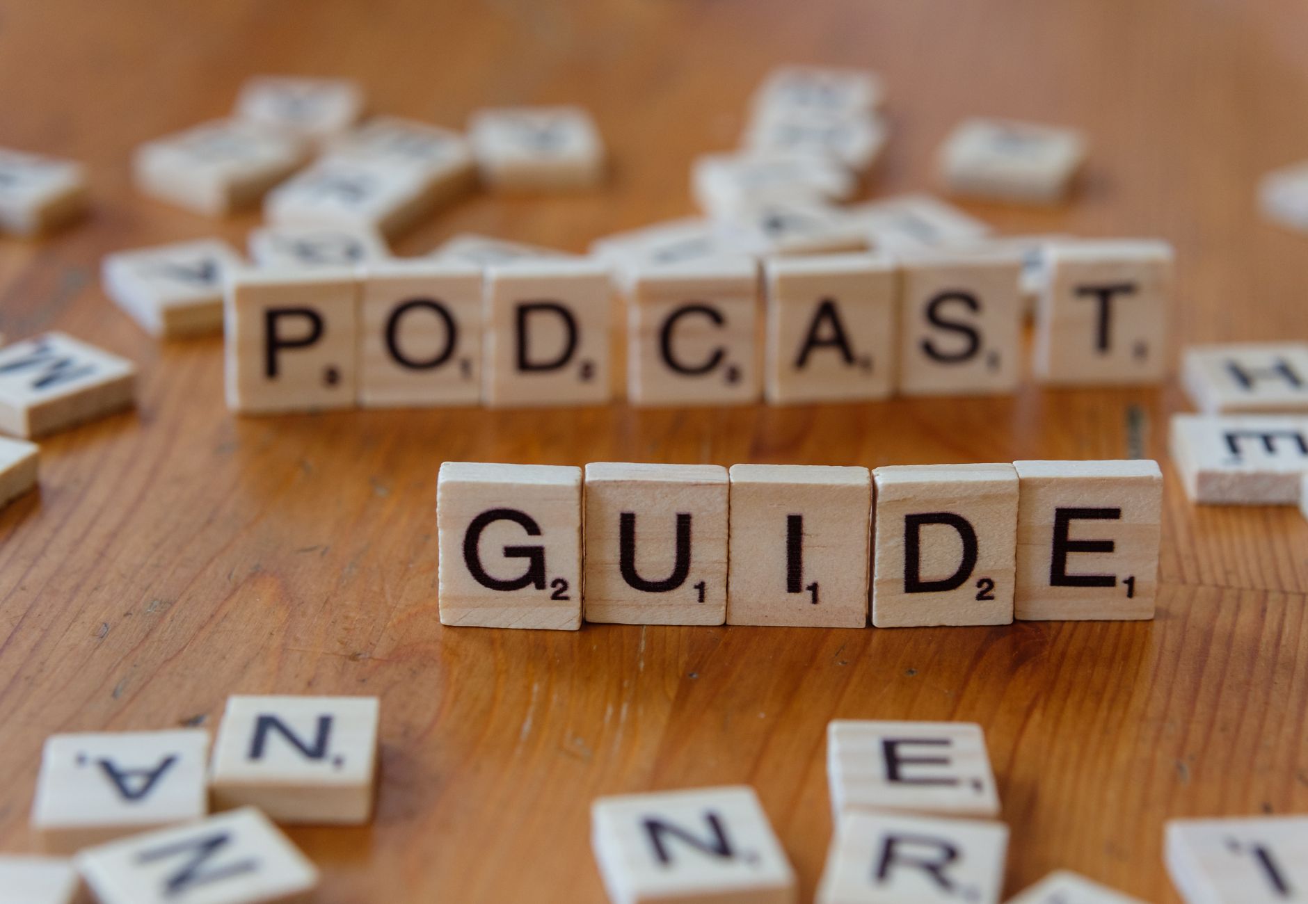 Scrabble tiles forming the words 'Podcast Guide' on a wooden surface.