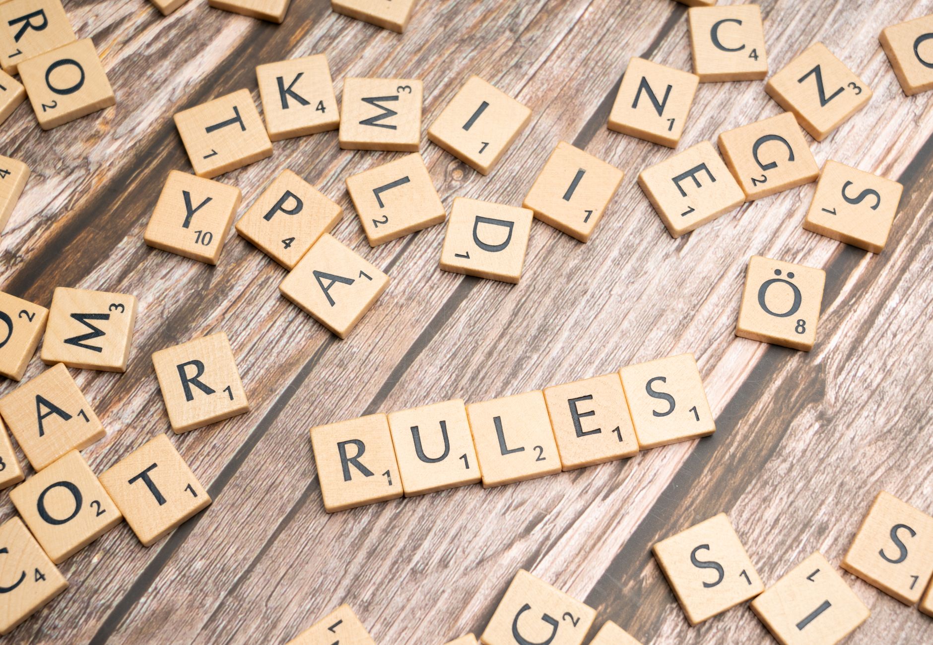 Wooden letter tiles arranged to spell 'Rules' on a textured wooden background.